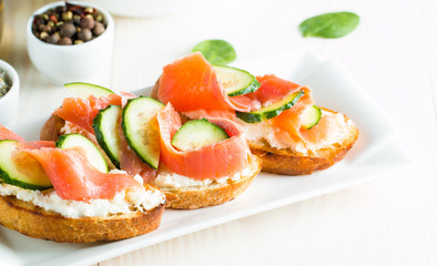 Salmon, cucumber and cream cheese bruschetta. Italian tapas, antipasti with vegetables, herbs and oil on grilled ciabatta and baguette bread. Sandwich.