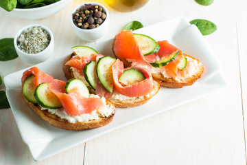 Salmon, cucumber and cream cheese bruschetta. Italian tapas, antipasti with vegetables, herbs and oil on grilled ciabatta and baguette bread. Sandwich.