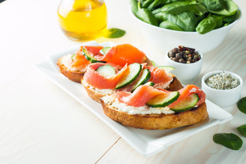 Salmon, cucumber and cream cheese bruschetta. Italian tapas, antipasti with vegetables, herbs and oil on grilled ciabatta and baguette bread. Sandwich.