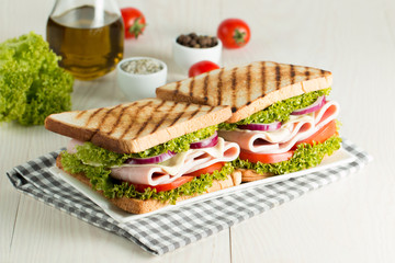 Close-up photo of a club sandwich. Sandwich with meat, prosciutto, salami, salad, vegetables, lettuce, tomato, onion and mustard on a fresh sliced rye bread on wooden background. Olives background.