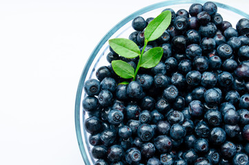  close-up of blueberries with leaves in a plate on a white background