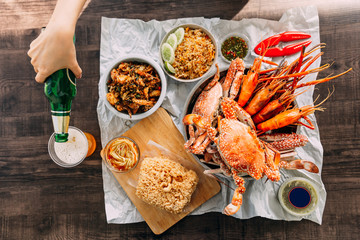 Top view of Steamed Giant Mud Crabs, Grilled Prawns (Shrimps), Crab Fried RIce, Pepper and Garlic Soft-Shell Crab, Crispy Catfish, Mango Salad and Thai spicy seafood sauce. Served with Beer.