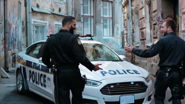 Two young men cops sit in patrol car walk pistol run enforcement happy officer police uniform auto safety security communication control policeman close up slow motion