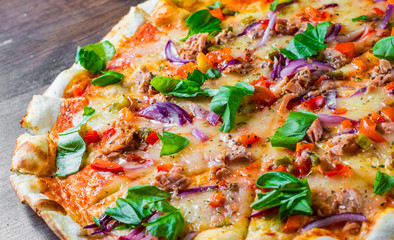 Pizza with Mozzarella cheese, onion,  tuna fish, tomato sauce, pepper, basil. Italian pizza on wooden table background
