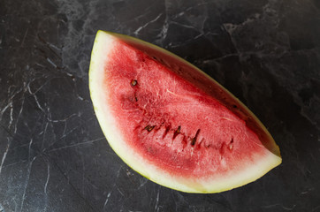 Fototapeta na wymiar A piece of ripe watermelon on a dark gray kitchen countertop. Place for text. The concept of ripening summer fruits and berries, vitamin food. Flat lay, minimalism.