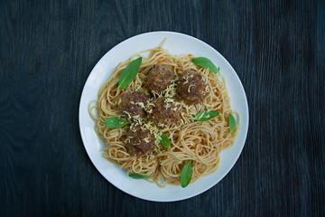 Pasta with meatballs and parsley in tomato sauce. Dark wooden background. View from above.
