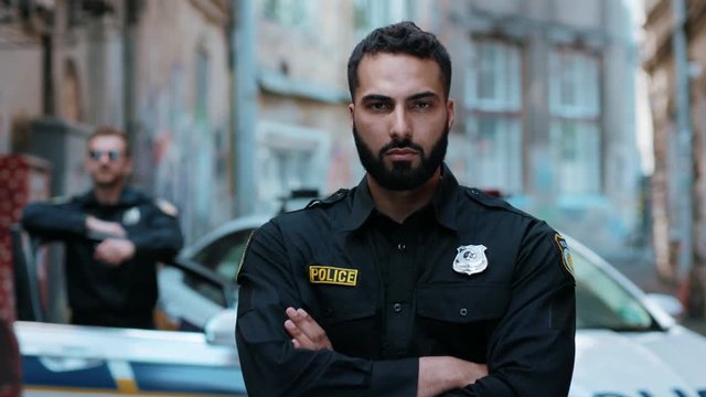 Handsome young man cops stand near patrol car look at camera serious enforcement officer police uniform auto safety security communication control policeman close up slow motion