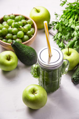Green smoothie in a cactus shaped glass among the green ingredients of apples, spinach, avocado and parsley. Healthy raw food and detox concept