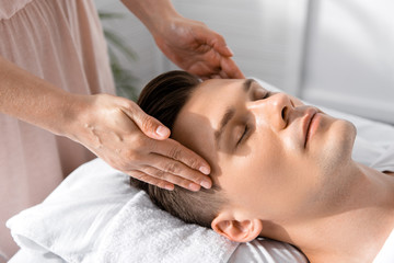 cropped view of masseur standing near man with closed eyes and touching his head