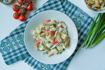 Salad with crackers, crab sticks, chicken fillet, fresh herbs and hard cheese seasoned with mayonnaise butter served in a white plate. Salad with mayonnaise. View from above. White background.