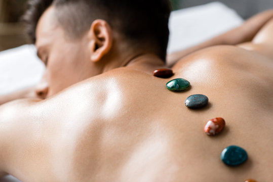 selective focus of shirtless man with colorful stones on his back