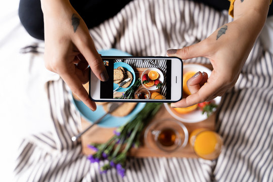 Woman sitting on bed, taking smartphone pictures of her healthy breakfast