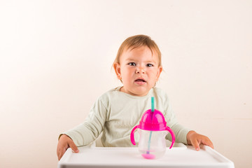 Baby toddler with sipping cup with straw. Baby water. Unhappy face. Isolated