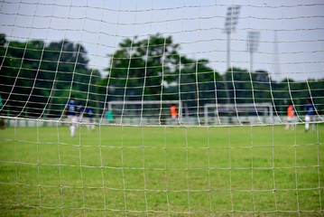 Boys are playing soccer in soccer field, Picture is captured behind soccer goal.