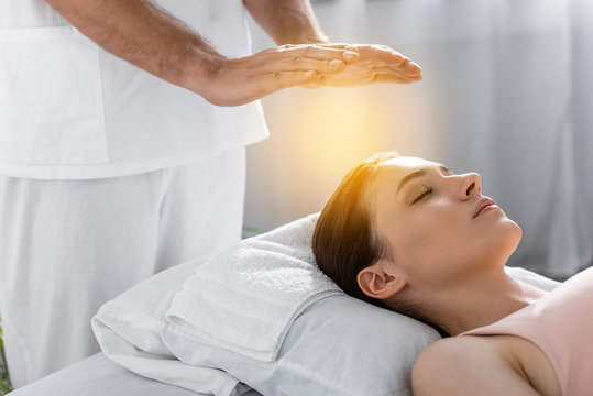 cropped view of healer standing near patient on massage table and cleaning aura