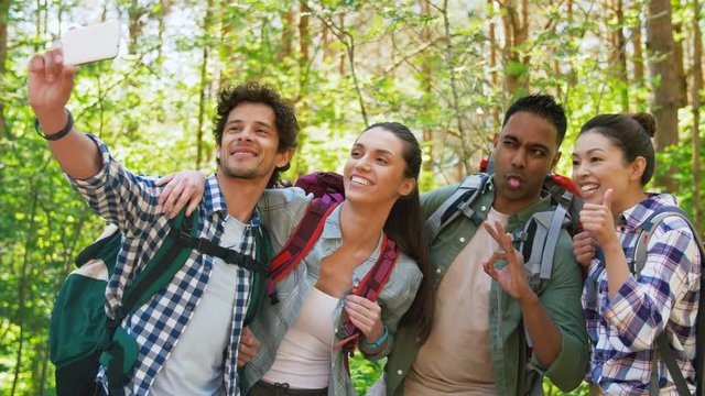 travel, tourism, hike and people concept - group of friends with backpacks taking selfie by smartphone in forest