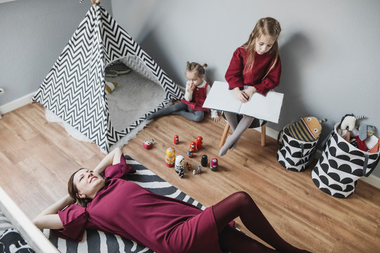 Mother relaxing with two girls in children's room at home