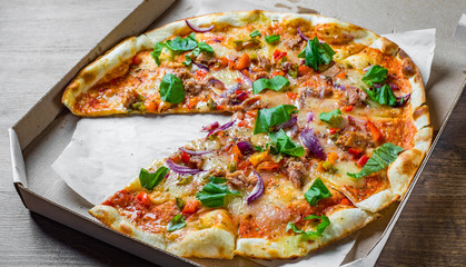 Pizza with Mozzarella cheese, onion,  tuna fish, tomato sauce, pepper, basil. Italian pizza in the in delivery cardboard box on wooden table background