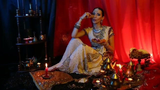 Beautiful young indian woman in traditional Sari clothing and Oriental Jewelry eating oriental sweets.