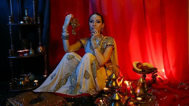 Beautiful young indian woman in traditional Sari clothing and Oriental Jewelry eating sweet grapes.