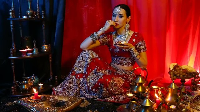 Beautiful young indian woman in traditional Sari clothing and Oriental Jewelry eating oriental sweets.
