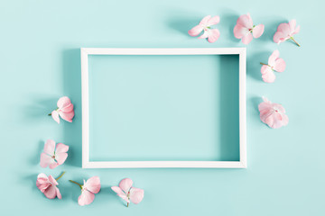 Beautiful flowers composition. Light pink flowers, empty photo frame for text on pastel blue background. Wedding. Birthday. Valentines Day. Mother's day. Flat lay, top view, copy space