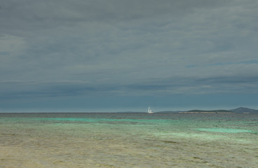 Cloudy Summer day on the Adriatic sea on the island Dugi otok, Long island. In the distance, a white sailboat is sailing along the sea. Photo in gray, blue and green shades.