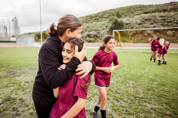 Coach embracing smiling girl on soccer field © Cavan for Adobe