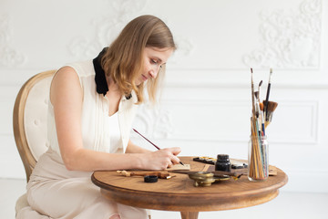 An attractive female artist sits at a table in an art workshop and draws a sketch of a drawing.