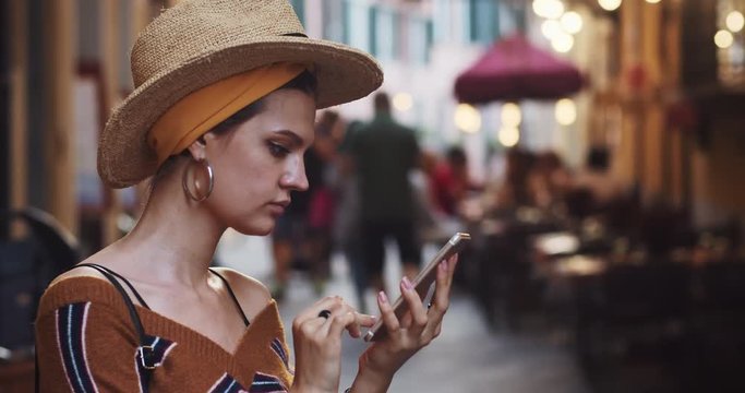 Profile of pretty busy young woman using smartphone staying outdoors. Attractive sociable girl with mobile device in beautiful italian city. Summer travel. Lucca, Tuscany, Italy.