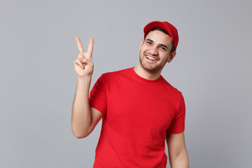 Delivery man in red uniform workwear isolated on grey wall background, studio portrait. Professional male employee in cap t-shirt print working as courier dealer. Service concept. Mock up copy space.