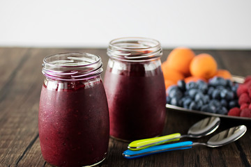 Fruit and berry smoothies and fresh apricots, raspberries and blueberries on an oval metal plate. Gray background.