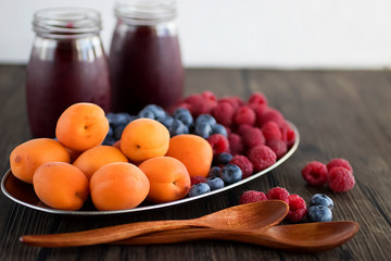 Fruit and berry smoothies and fresh apricots, raspberries and blueberries on an oval metal plate. Gray background.