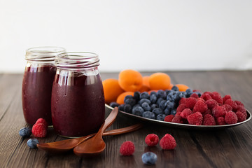 Fruit and berry smoothies and fresh apricots, raspberries and blueberries on an oval metal plate. Gray background.