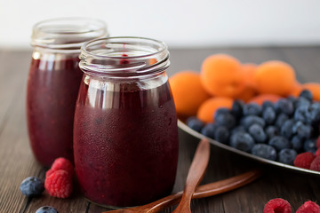 Fruit and berry smoothies and fresh apricots, raspberries and blueberries on an oval metal plate. Gray background.