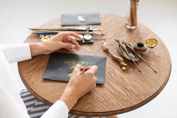 Woman calligrapher is holding a pen with ink and signs a card in handwritten font. Close-up. Soft...