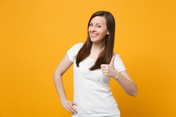 Portrait of smiling successful young woman in white casual clothes looking camera, showing thumb up isolated on bright yellow orange background in studio. People lifestyle concept. Mock up copy space.