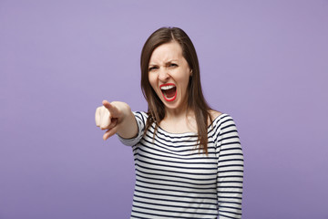 Angry young woman in casual striped clothes posing isolated on violet purple background in studio. People lifestyle concept. Mock up copy space. Screaming, swearing, pointing index finger on camera.