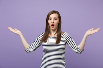 Shocked young woman in casual striped clothes posing isolated on violet purple background in studio. People lifestyle concept. Mock up copy space. Keeping mouth open, spreading, pointing hands aside.