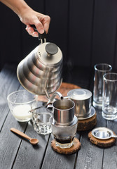 Making Vietnamese drip coffee. Woman hand pouring hot water into phin from goose neck kettle on black background