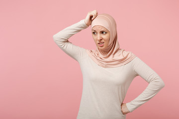 Preoccupied young arabian muslim woman in hijab light clothes posing isolated on pink background, studio portrait. People religious Islam lifestyle concept. Mock up copy space. Putting hand on head.