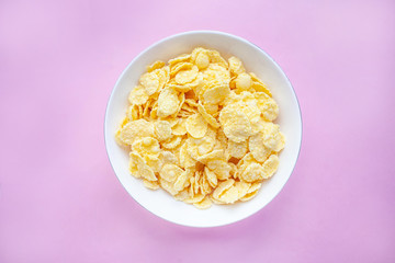 Cornflakes dry breakfast in a white bowl on a pink backgroud. top view