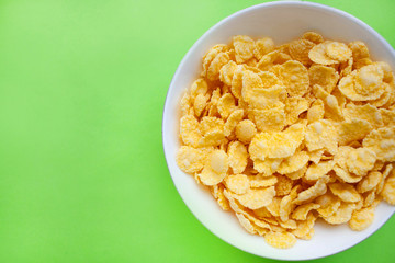 Cornflakes dry breakfast in a white bowl on a green backgroud. space for text