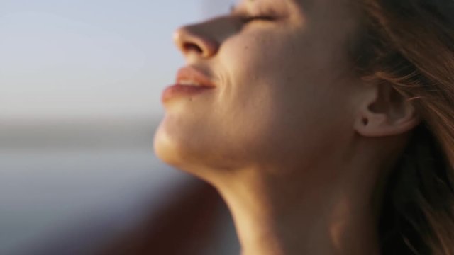 closeup face of young pretty woman enjoying peaceful sunset and looking ahead. hair flowing in the wind. calm and relaxation. slow motion Full HD stock footage.