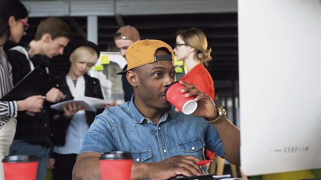 Concentrated afro american man in casual clothing working on computer, receiving unexpected email while drinking coffee or tea Serious freelance man thinking at office workplace