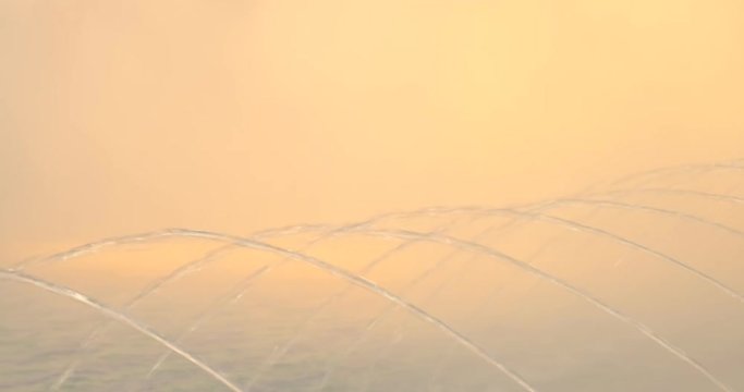 Detail and pattern of water fountain springs with misty vapors in the back, lit by the warm, coral / orange, sunset light. Concept for purity. 4K DCI.