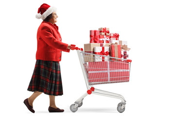 Elderly woman with a santa claus hat walking with a shopping cart with presents