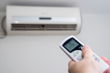 Hand with remote control directed on the conditioner on the wall. Air conditioner with remote controller