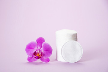 Cotton sponges in a glass jar on a pink background with an orchid flower