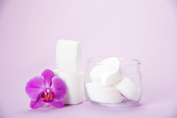 Obraz na płótnie Canvas Cotton sponges in a glass jar on a pink background with an orchid flower